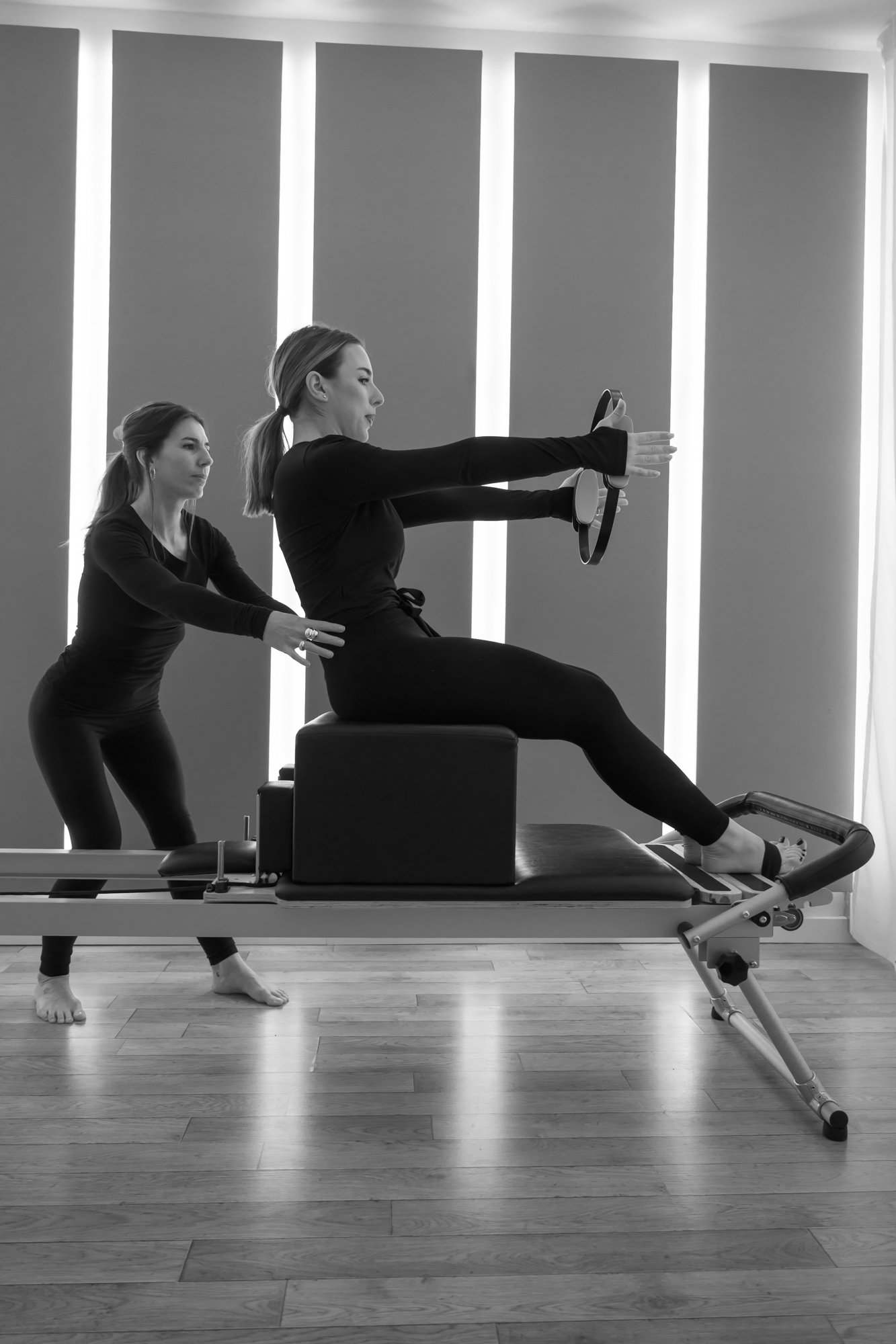 Marion accompagne une élève sur le Reformer, bras tendus vers un cercle de Pilates