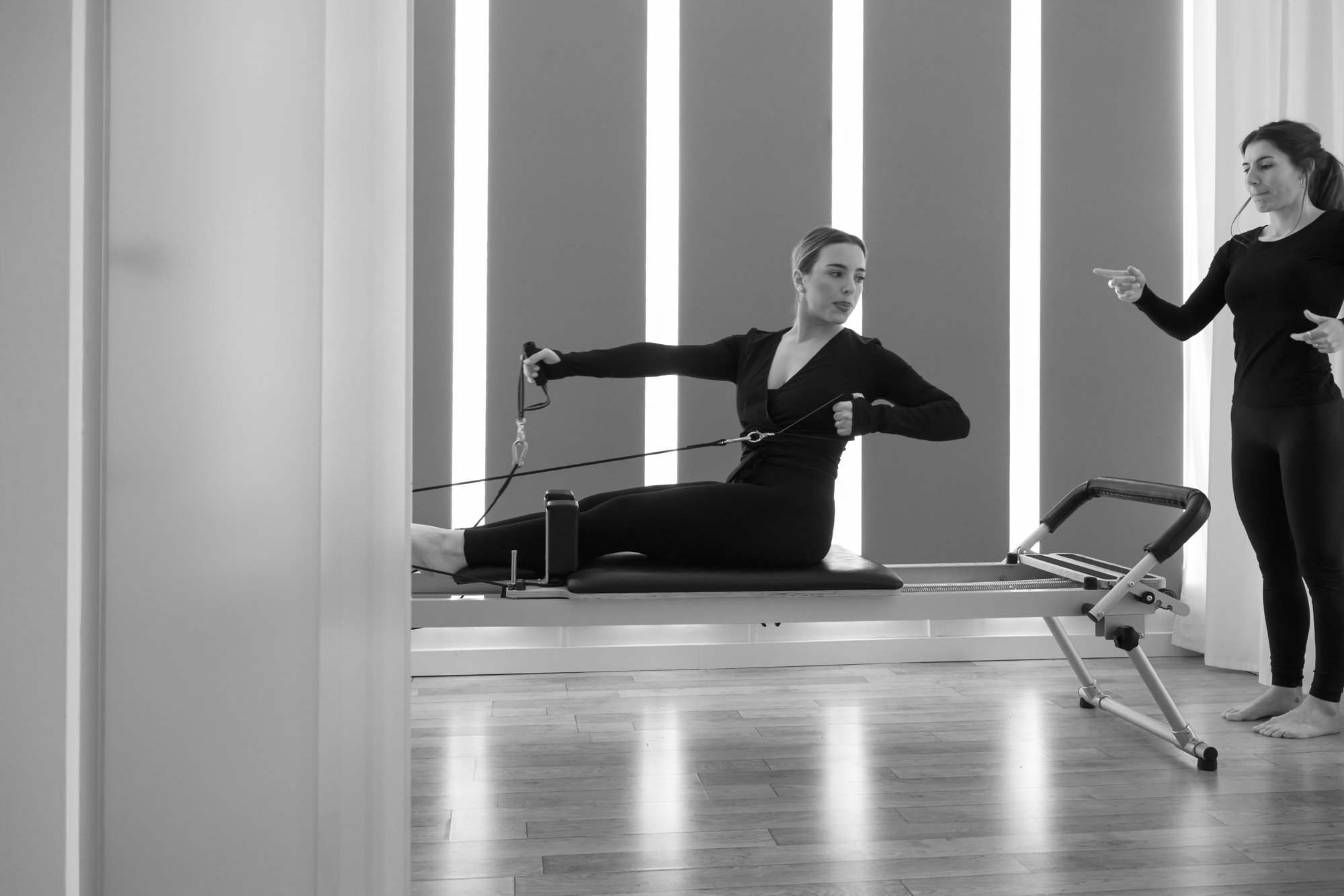 Marion guide une élève assise sur le Reformer, qui tire sur les sangles